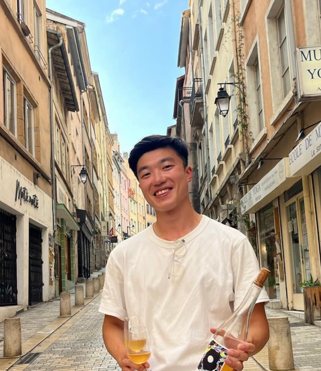 Eric Li holding a glass and bottle of wine on a city street